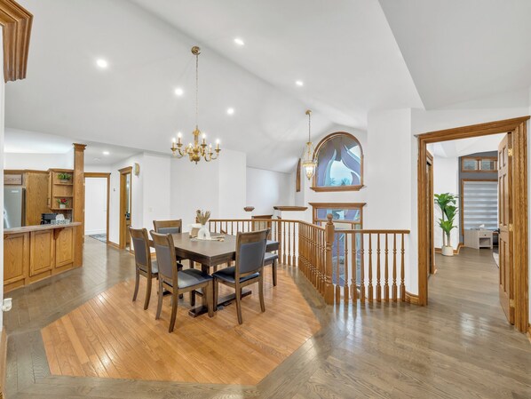 A spacious dining area with a wooden table and chairs, a chandelier, and a view of the kitchen and living areas.