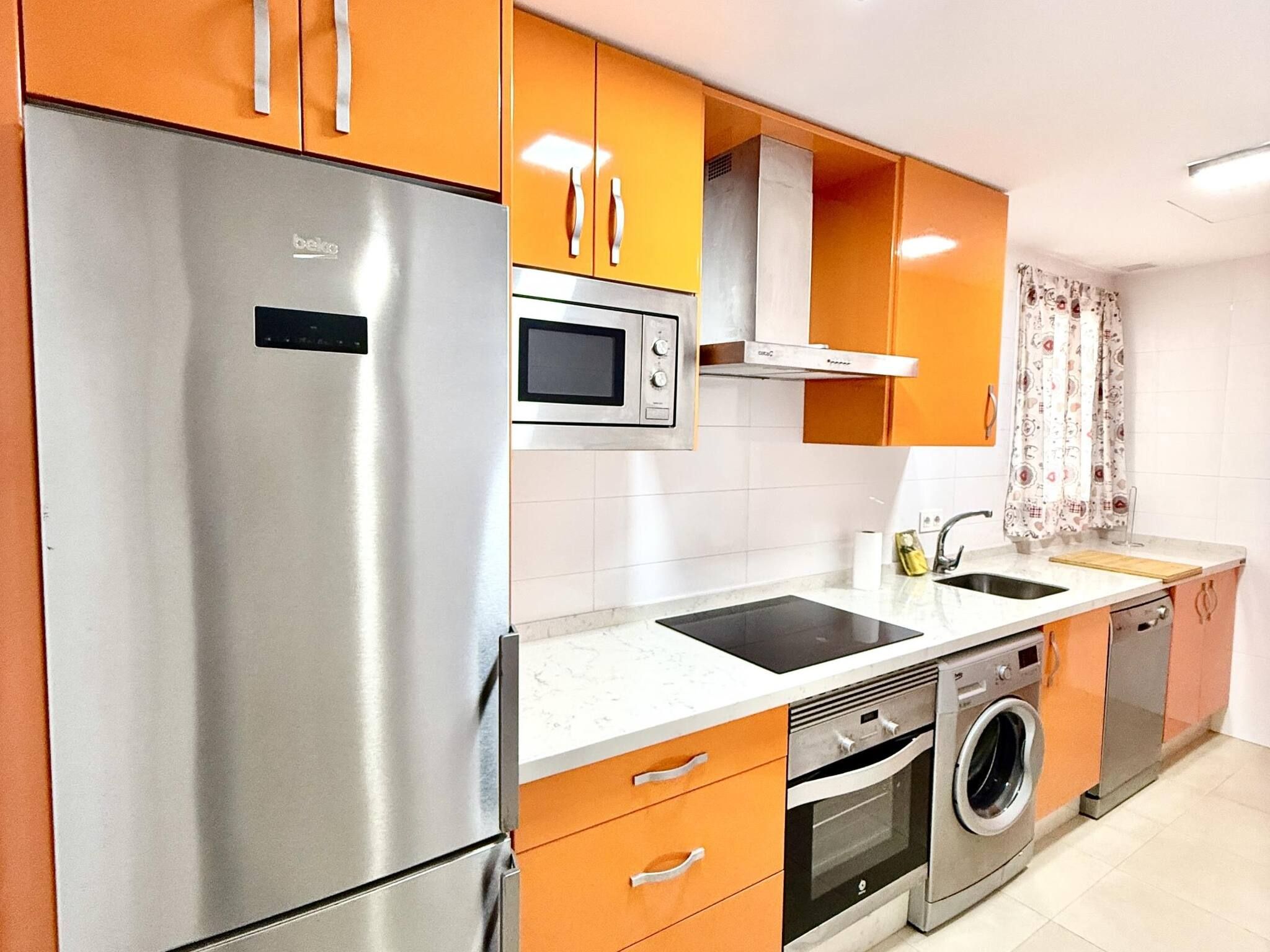 A modern kitchen with stainless steel appliances, a microwave, oven, and a washing machine.