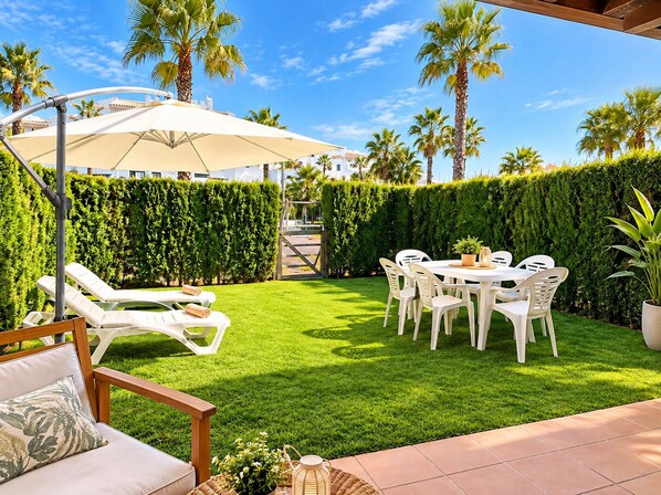 A well-maintained outdoor patio area with a dining table and chairs, a lounge chair, and a large umbrella.
