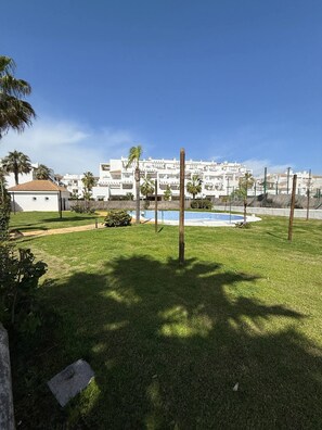 A residential area with a swimming pool, palm trees, and a white building with balconies.