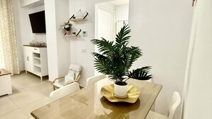 Un comedor con mesa de madera, sillas blancas, una planta en maceta y un televisor montado en la pared.