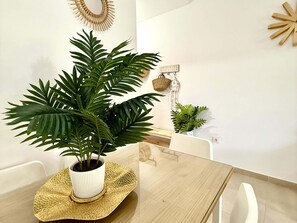 A dining area with a wooden table, white chairs, a potted plant, and a wall-mounted decorative item.