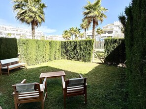 A backyard with a wooden table and chairs, a hedge, and palm trees.