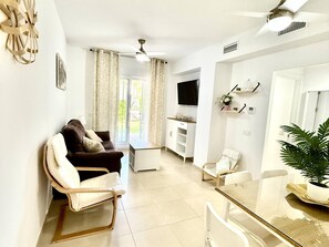 A living room with a sofa, a dining table, a TV, and a ceiling fan.
