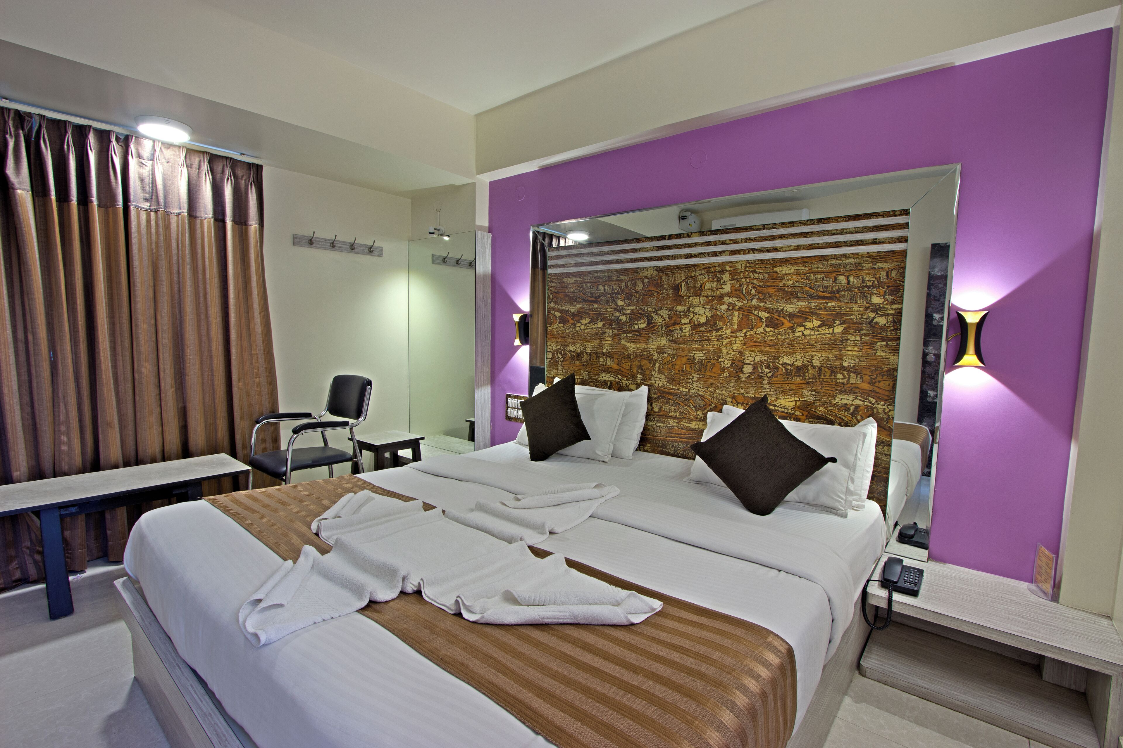 A hotel room with a large bed, a desk, a chair, and a bathroom with curtains.