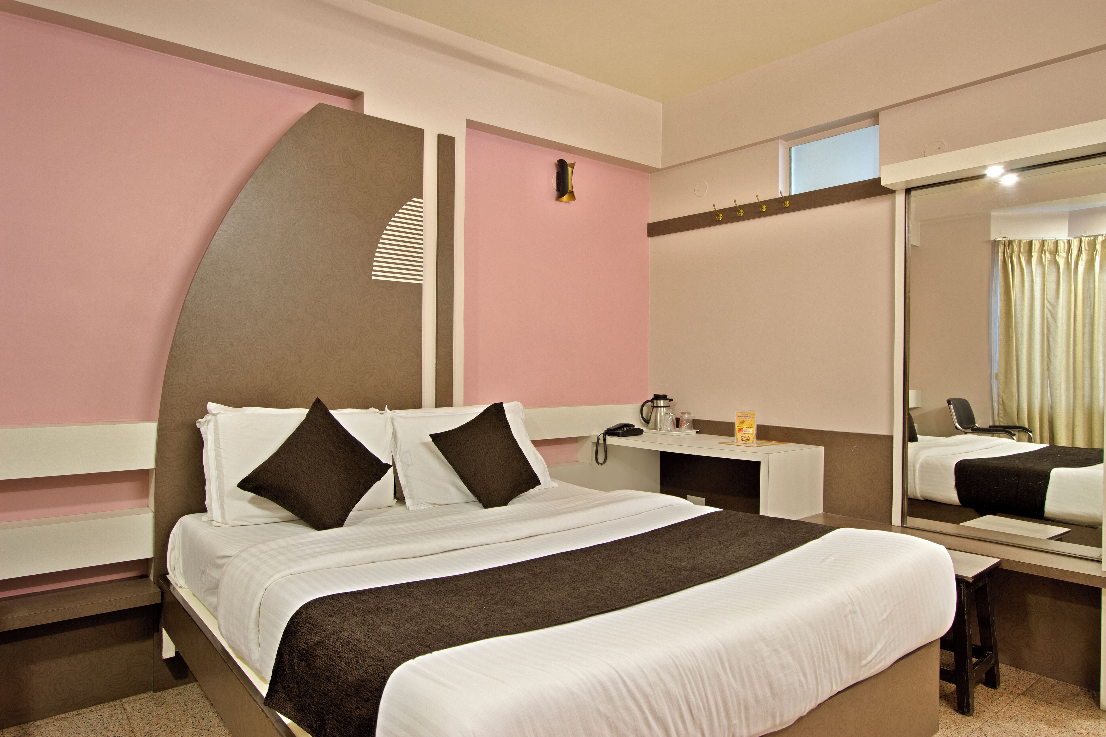A hotel room with a large bed, a desk, a chair, a mirror, and a window with curtains.