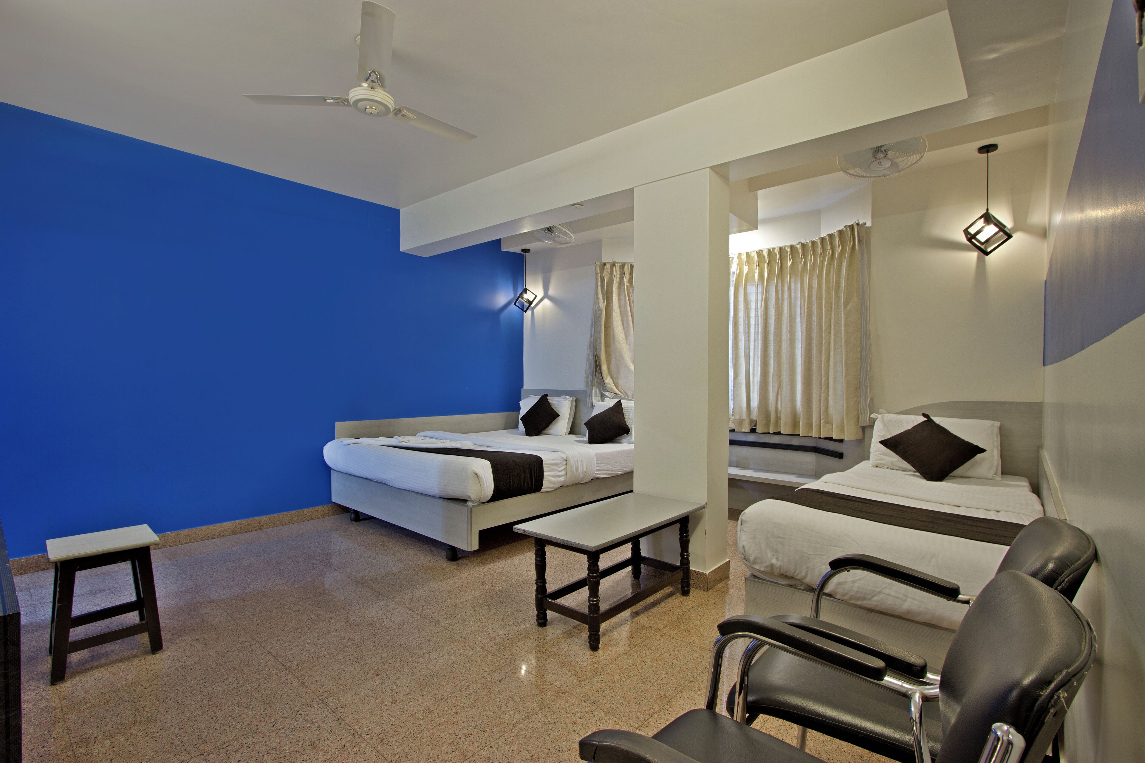A hotel room with two beds, a sofa, a small table, a chair, and a ceiling fan.