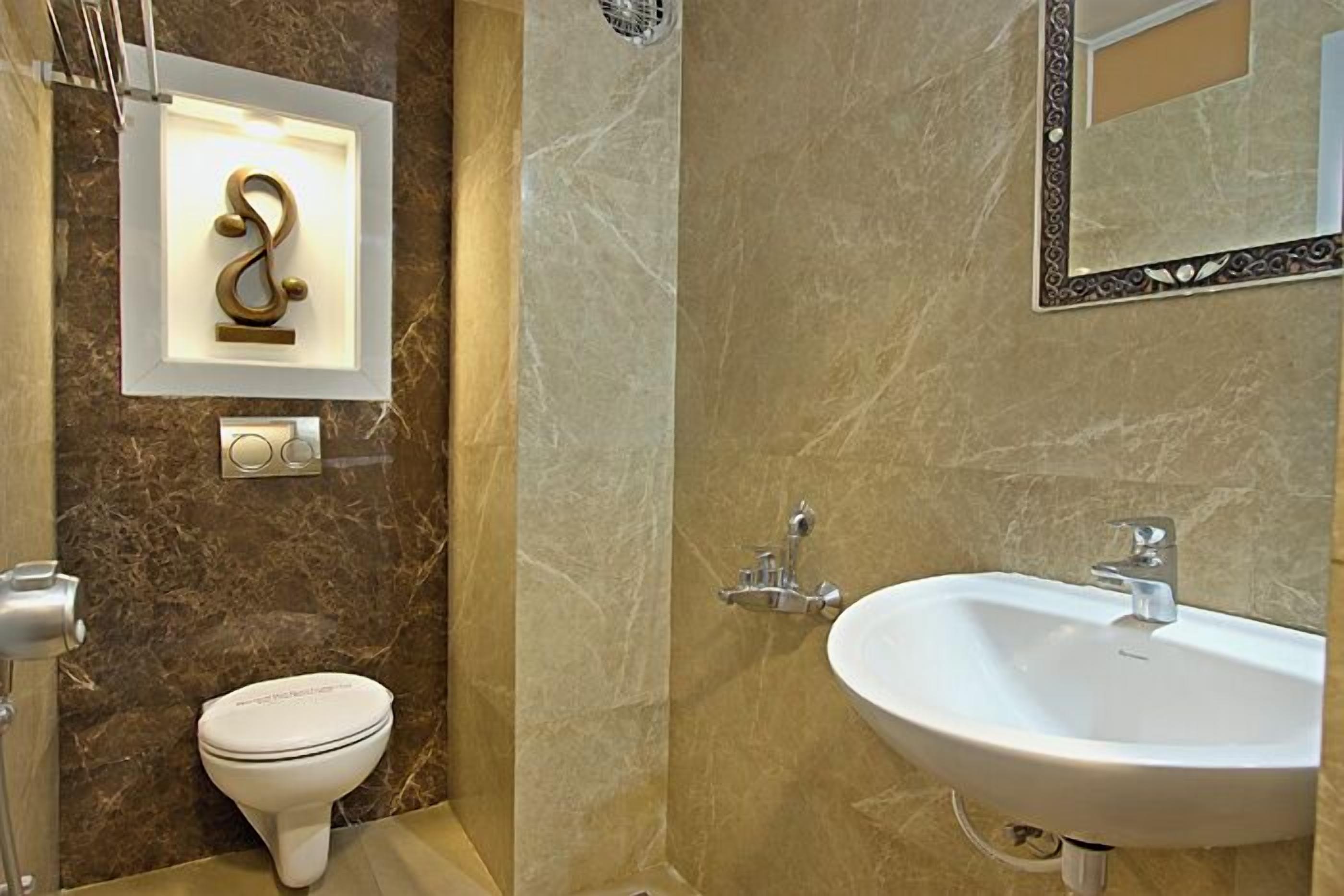 A bathroom with a marble wall, a white toilet, a sink, and a decorative wall piece.
