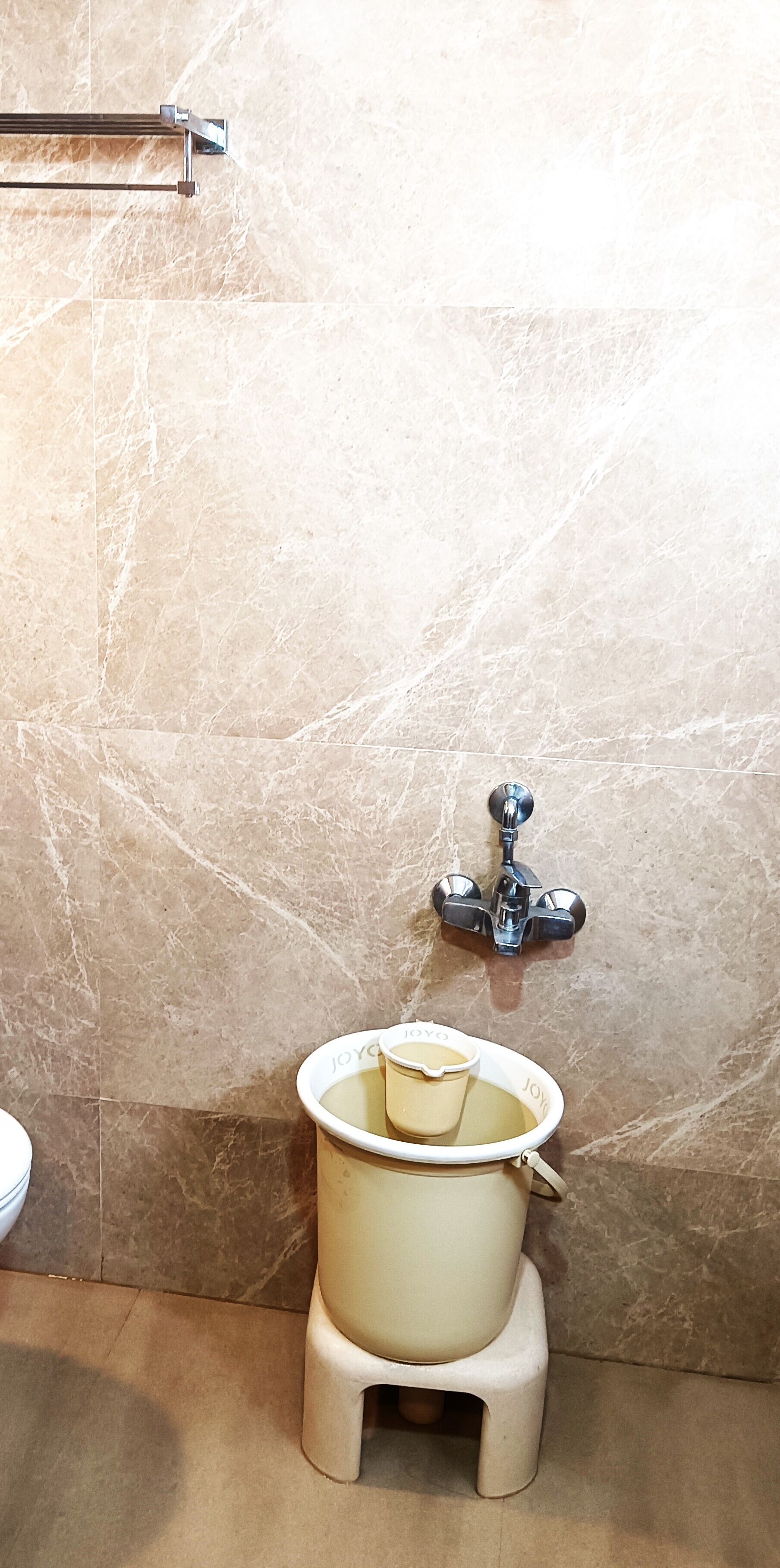 Un baño con pared de mármol, un inodoro y un taburete pequeño.
