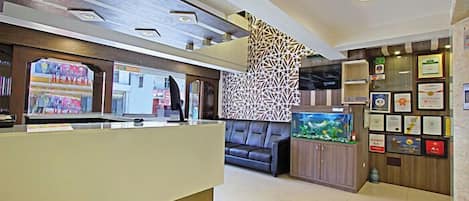 A hotel reception area with a modern design, including a reception desk, a sofa, a decorative wall, and a fish tank.