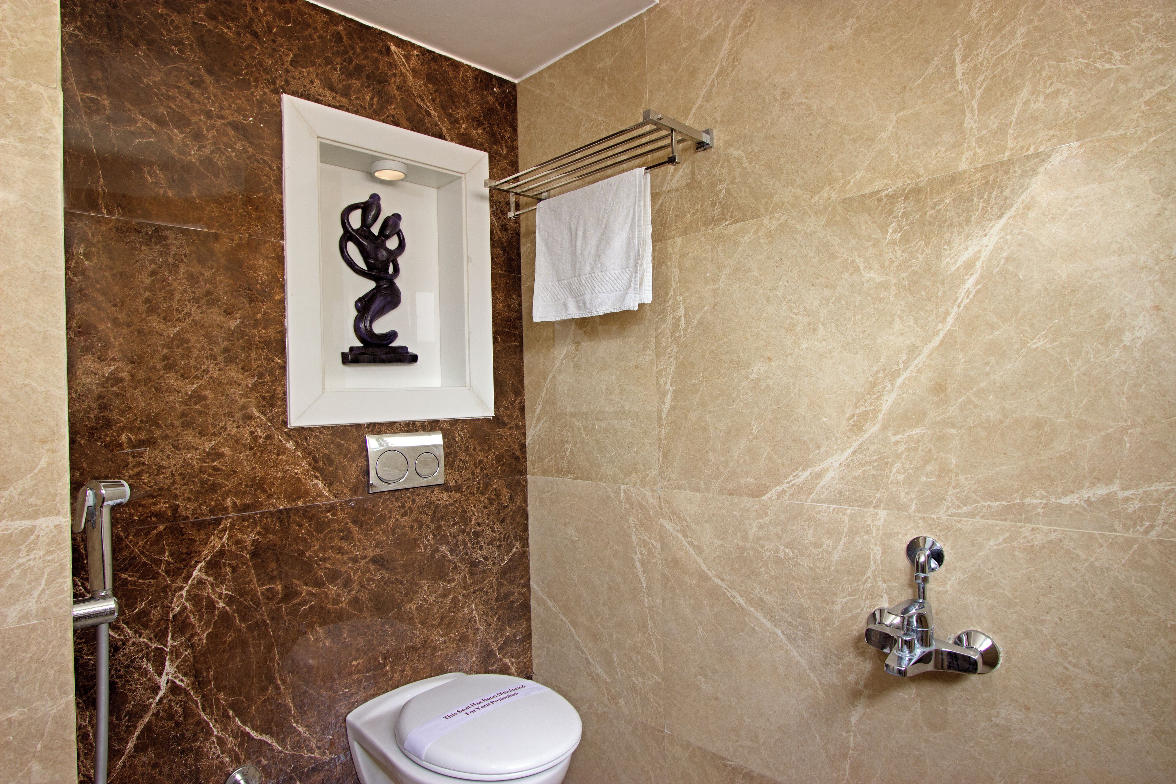A bathroom with a marble wall, a white toilet, a towel rack, and a shower with a chrome faucet.