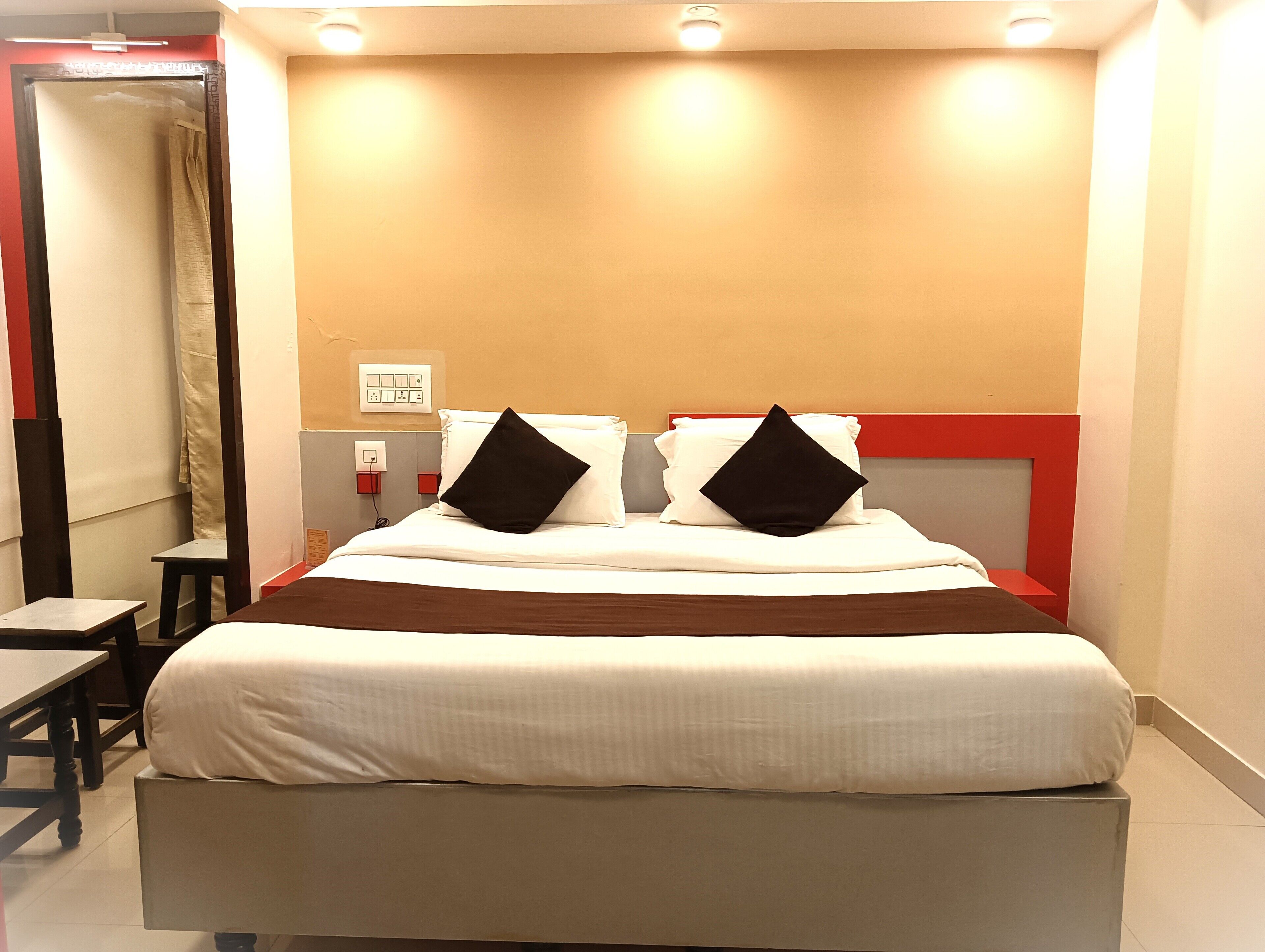 A hotel room with a large bed, two bedside tables, a nightstand, a red accent wall, and a ceiling light.