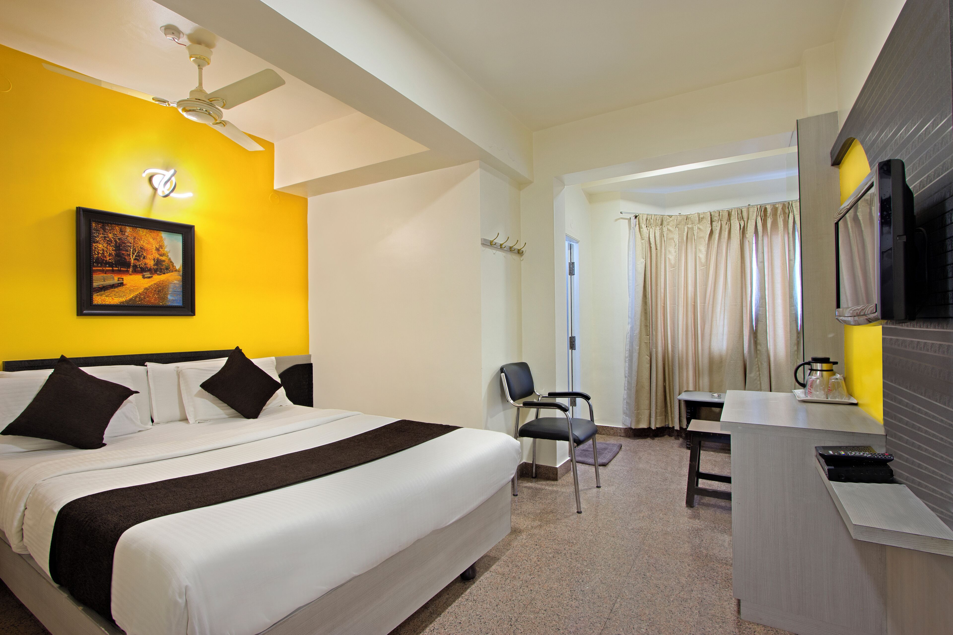 A hotel room with a bed, a desk, a chair, a television, and a ceiling fan.