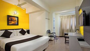 A hotel room with a bed, a desk, a chair, a television, and a ceiling fan.
