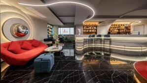 A modern lobby with a curved reception desk, a red sofa, and a blue ottoman. - Milegu Hotel (Changsha)