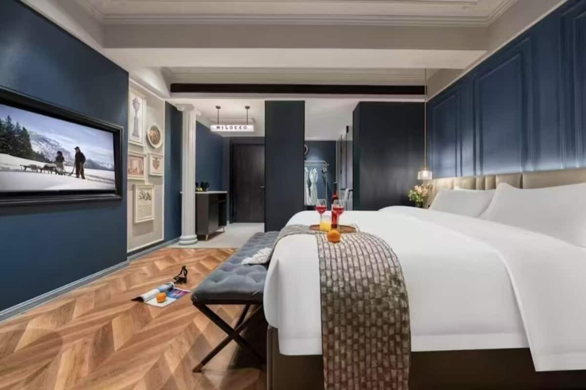 A hotel room with a large bed, a bench, a TV, and a desk.