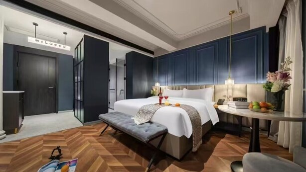 A modern hotel room with a large bed, a bedside table, a bench, and a small table with fruit. - Milegu Hotel (Changsha)