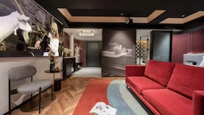 A modern living room with a red sofa, a patterned chair, and a large wall mural. - Milegu Hotel (Changsha)