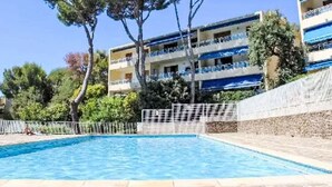 A swimming pool with a stone border, surrounded by trees and a building with balconies.