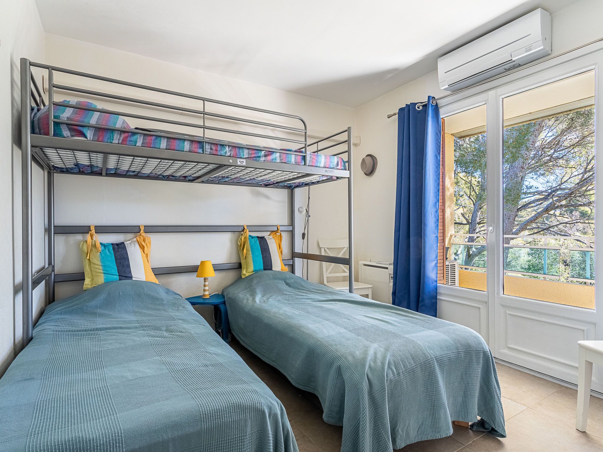 Een kamer met stapelbedden en twee eenpersoonsbedden, een tafeltje met een lamp en een raam met gordijnen.