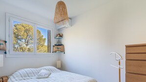 A bedroom with a bed, a window with a view of trees, a hanging light fixture, and a wooden dresser.