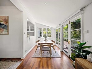 A dining area with a wooden table and chairs, a rug, and a view through large glass doors to an outdoor garden. - Newberry Cottage: Beach, Games & Alfresco Bliss (Dunsborough)