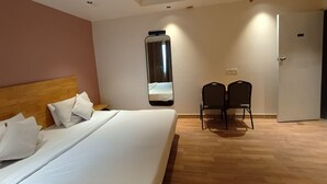 Habitación de hotel con una cama grande, cabecera de madera, dos sillas, un espejo y una puerta.