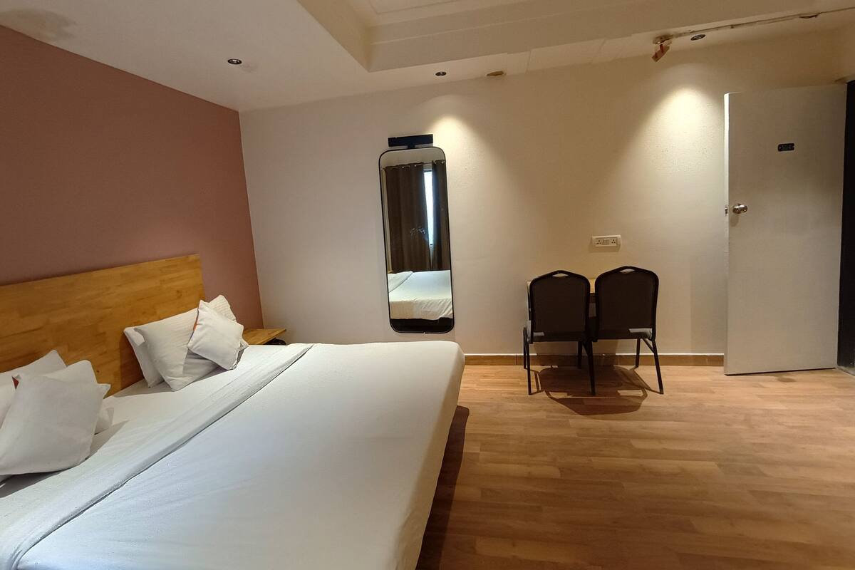 A hotel room with a large bed, a wooden headboard, two chairs, a mirror, and a door.