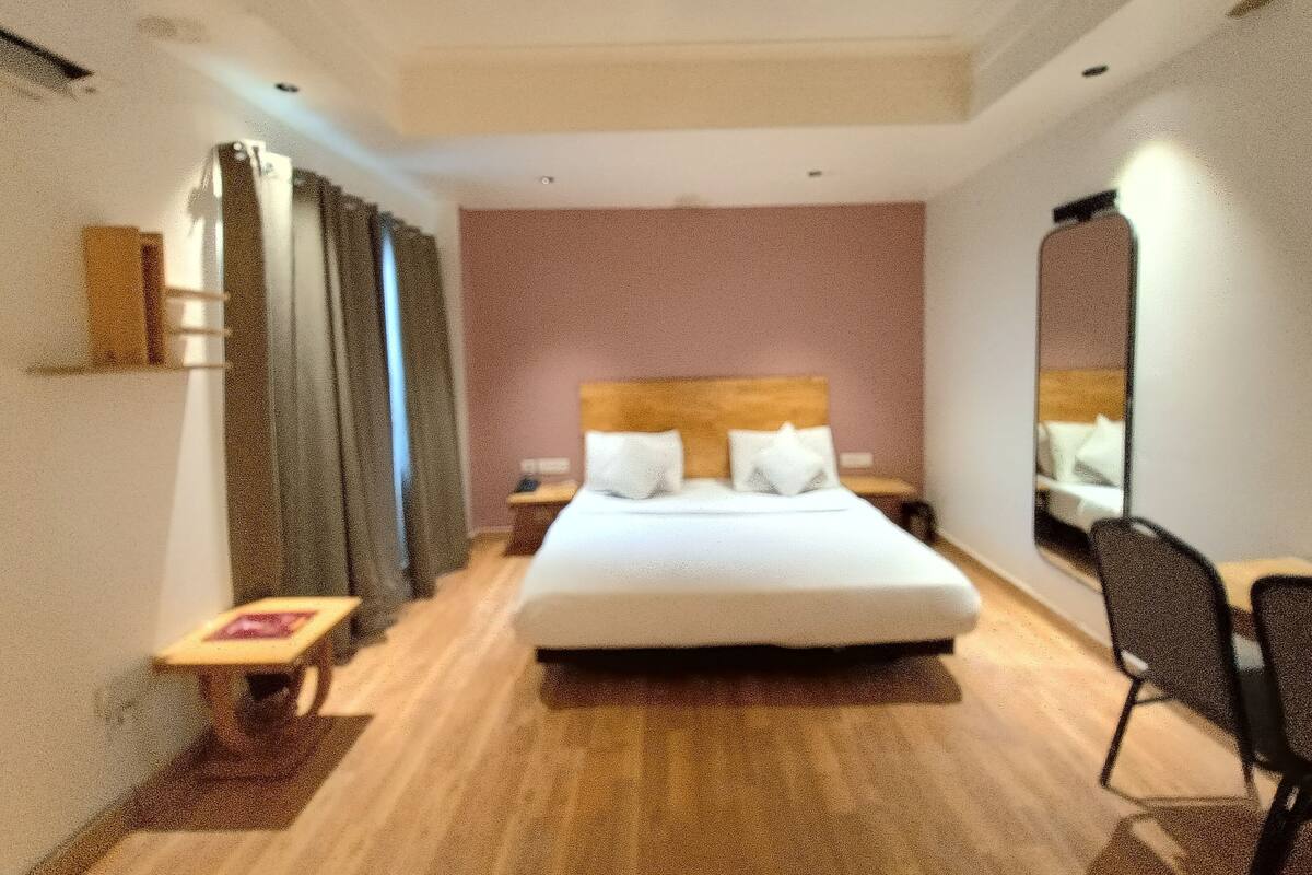 A hotel room with a large bed, a bedside table, a chair, and a mirror.