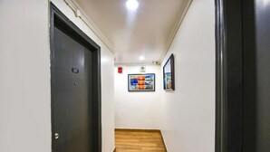 Un pasillo con suelo de madera, una puerta negra a la izquierda y un cuadro en la pared.
