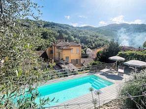 A pool area with a view of a hillside villa, outdoor furniture, and a clear sky.