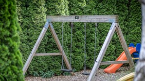 Un ensemble de balançoires en bois installé dans un jardin, avec une haie verte en arrière-plan.