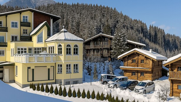 Une station de ski avec des bâtiments à plusieurs étages, un parking et des arbres couverts de neige.