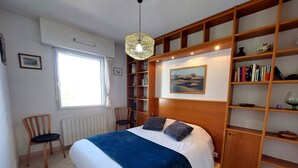A bedroom with a large bed, a wooden bookshelf, a desk, and a chair.