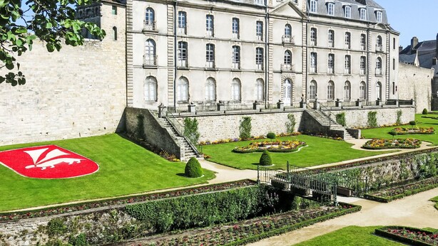 A large, historic building with a symmetrical facade, multiple windows, and a central staircase leading to a gated entrance.