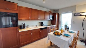 A modern kitchen with wooden cabinets, a built-in oven, and a dining area with a table set for two.