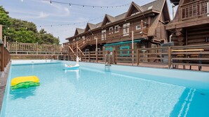 A pool area with wooden buildings, a lifeguard chair, and a floating toy. - Daecheon Ocean Forest Pension (Boryeong)