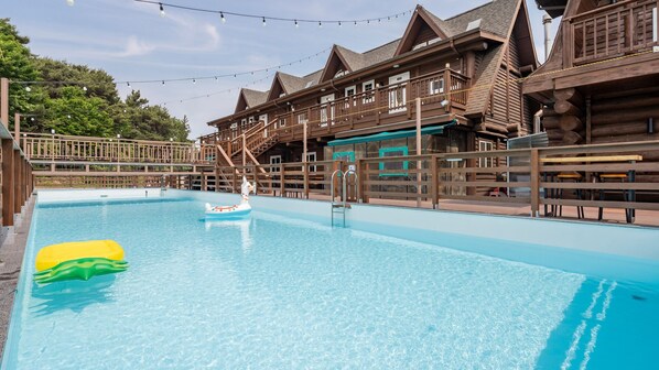 A pool area with wooden buildings, a lifeguard chair, and a floating toy. - Daecheon Ocean Forest Pension (Boryeong)
