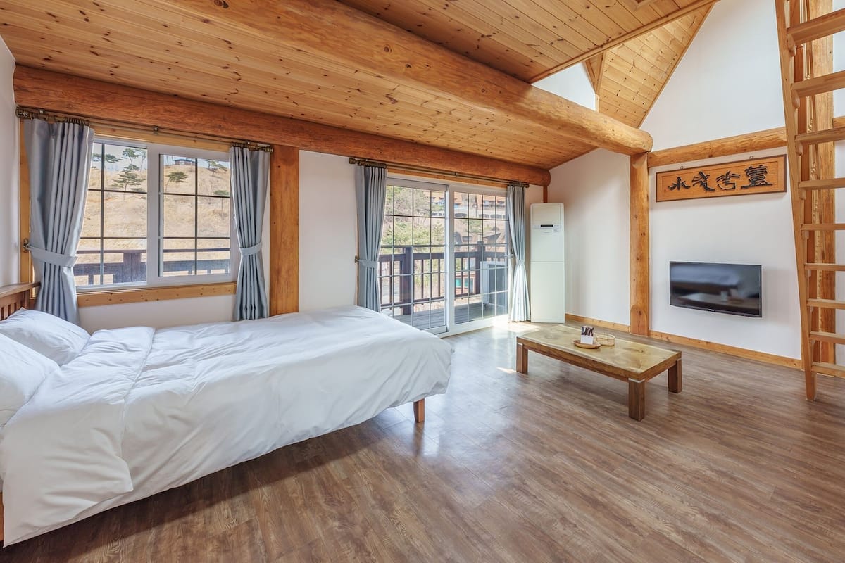 Una habitación con una cama, televisión, mesa de madera y vistas al exterior.