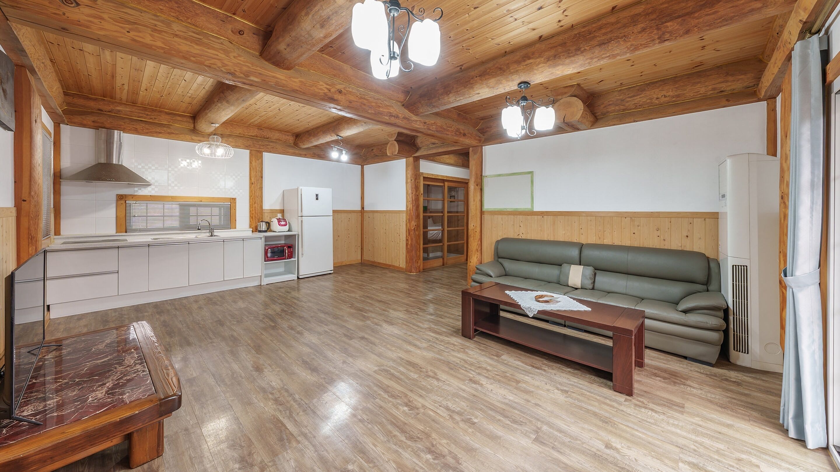Amplia sala de estar con techo de madera, un sofá, una mesa de centro y una zona de cocina con refrigerador y microondas.