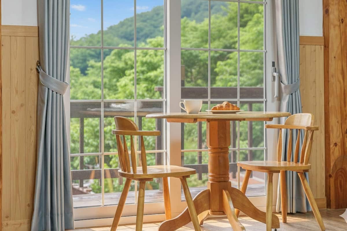 Una habitación con estructura de madera y un ventanal grande con vistas a un área boscosa.
