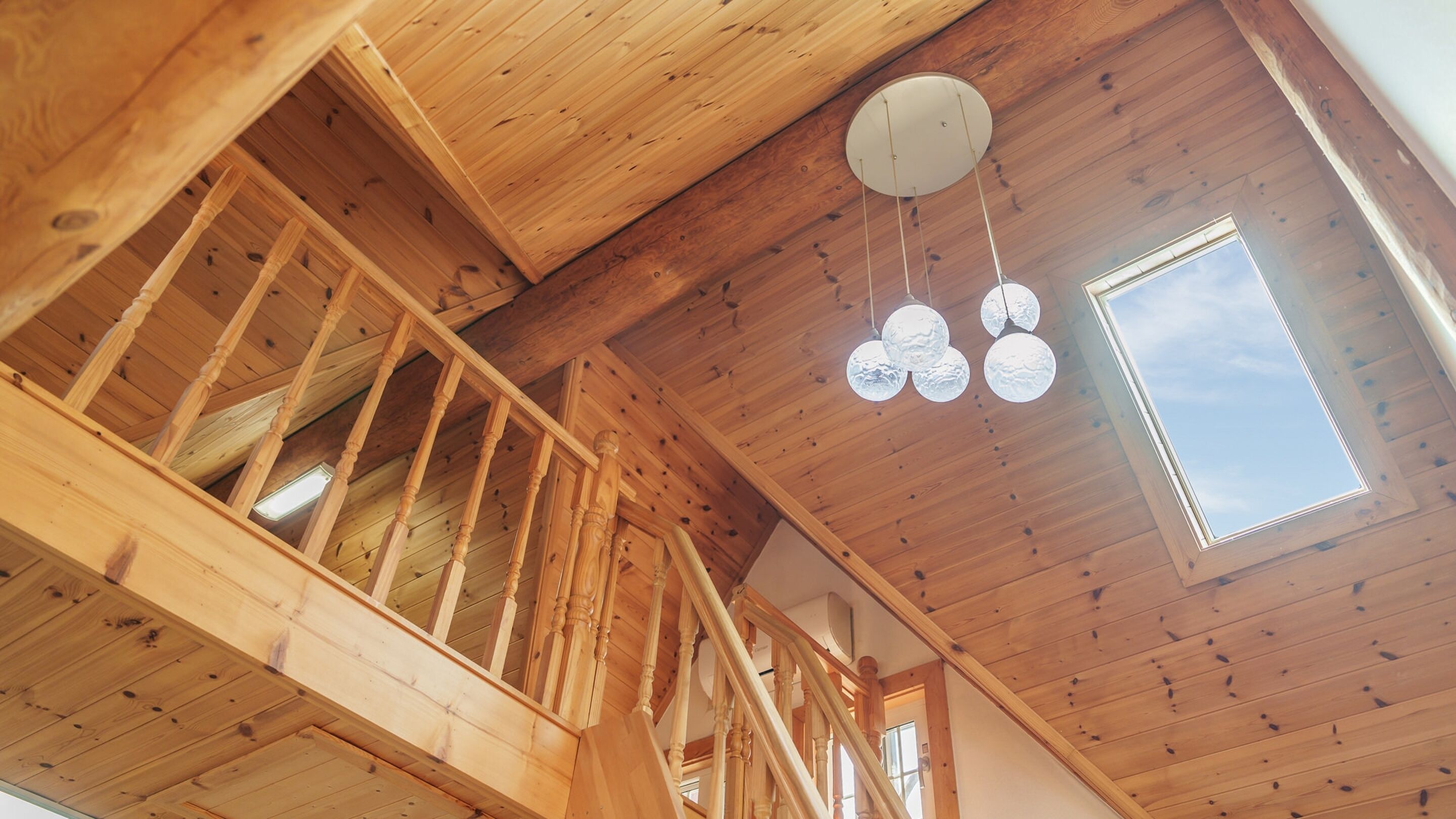 A wooden interior with a staircase, a skylight, and a hanging light fixture.