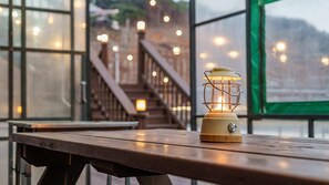 A wooden table with a lantern on it, a staircase in the background, and large windows with lights. - Daecheon Ocean Forest Pension (Boryeong)