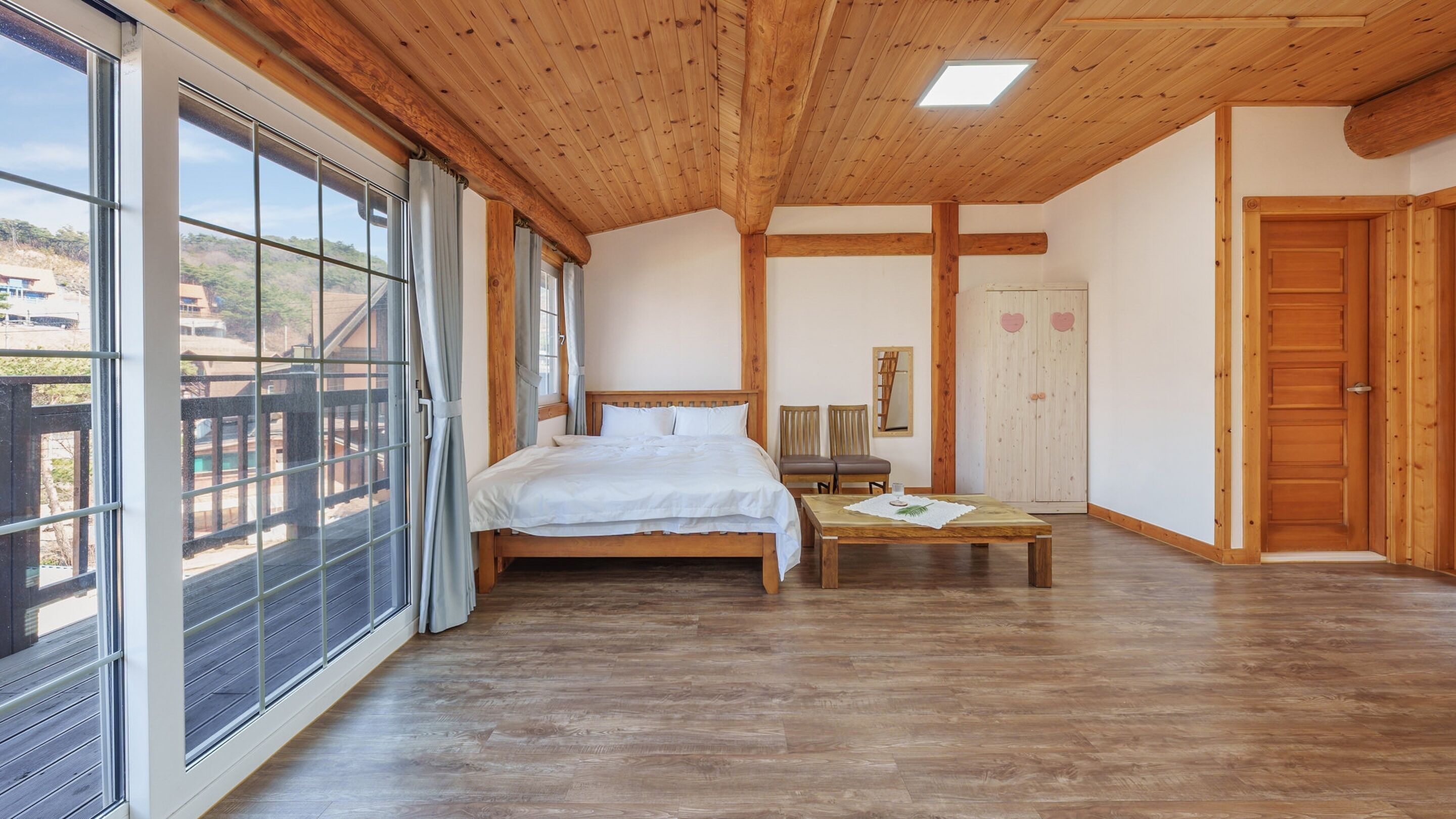 A spacious bedroom with a large bed, a wooden ceiling, and a view through large windows.