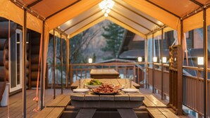 A covered outdoor dining area with a table set for a meal, surrounded by wooden railings and a view of trees. - Daecheon Ocean Forest Pension (Boryeong)