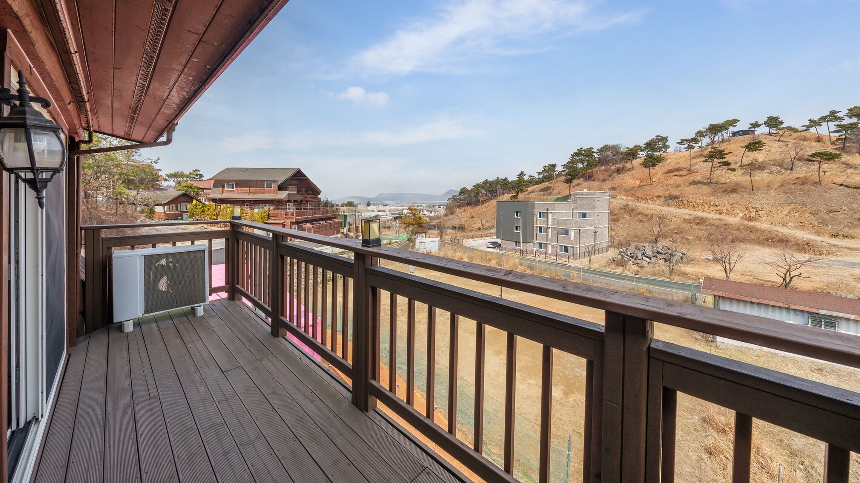 A wooden deck with a view of a residential area, including houses and a hill with trees.