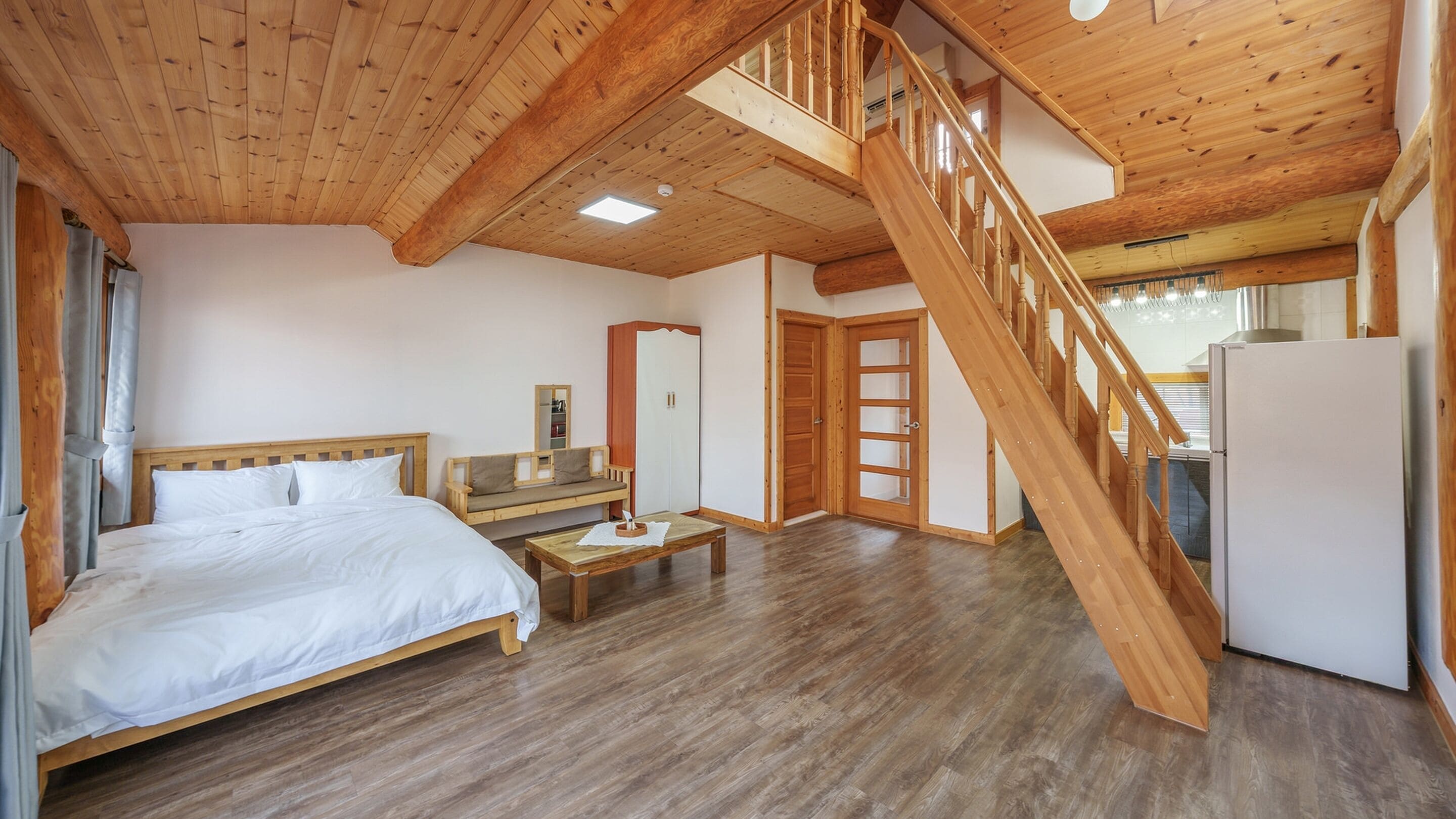 Amplia habitación con piso de madera, una cama, un sofá, una mesita y una escalera que lleva a otro nivel.