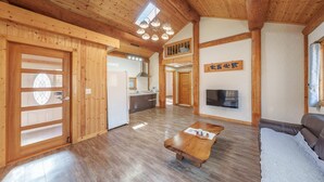 A spacious living area with wooden floors, a central coffee table, a sofa, a TV mounted on the wall, and a kitchen in the background. - Daecheon Ocean Forest Pension (Boryeong)
