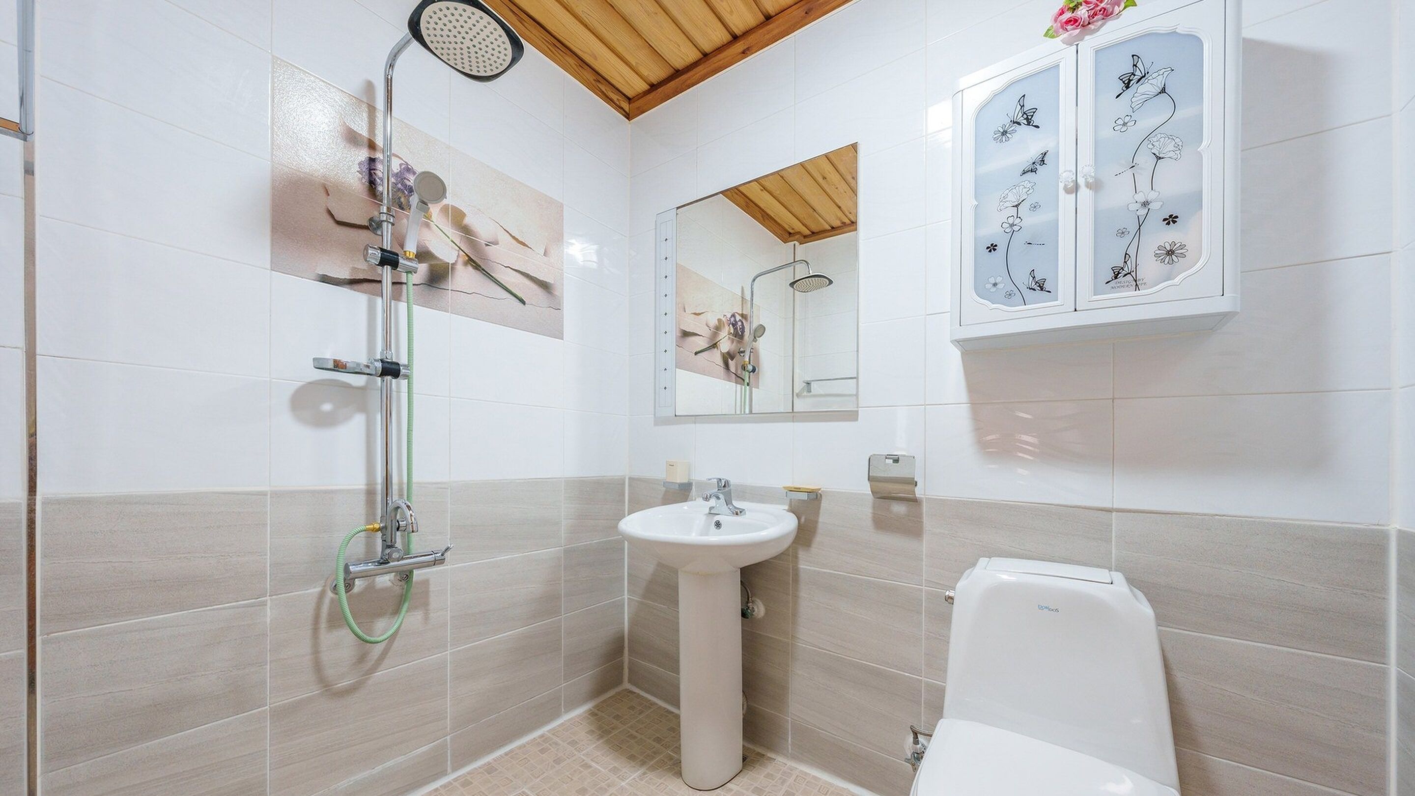 A bathroom with a shower, sink, toilet, and a cabinet with floral designs.