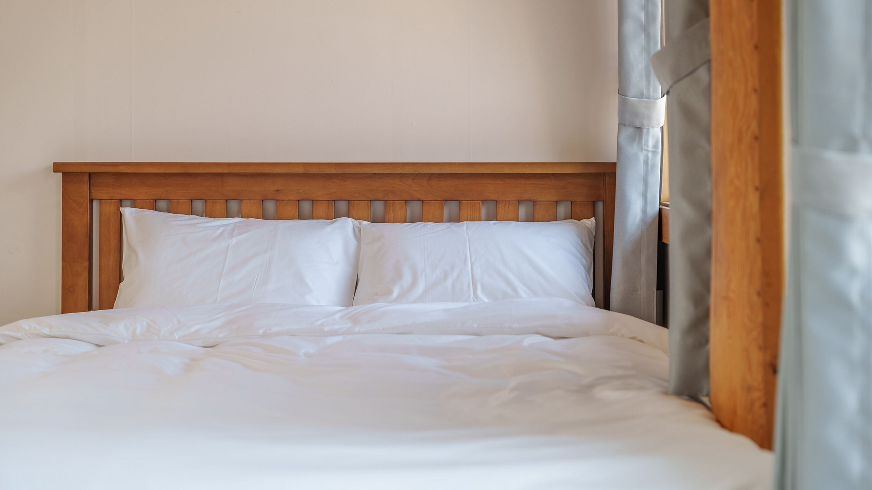 Cama bem arrumada com lençóis brancos e cabeceira de madeira.
